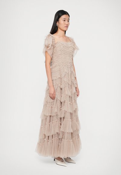 Pikk, mitme tasandiga kleit, mis on valmistatud läbipaistvast beežist tüllist ja kaunistatud volangidega. Omab puffvarrukaid ja ruudukujulist dekolteed. Kandetud teravapatjadega valgete kontsadega.