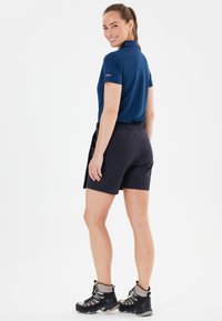 Marinblå polo skjorta och svarta shorts, kombinerat med svarta vandringskängor. Kortsleeves, elastisk midja och strukturerat material.