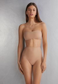 Huidskleurige strapless bandeau-top en high-waisted slips, gemaakt van een gladde stof met een naadloos ontwerp en een minimalistische stijl.