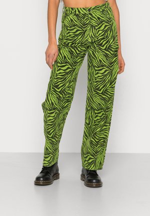 Calças largas de riscas verdes em formato de zebra, feitas de um tecido leve, com uma cintura alta e design de cinco bolsos. Botas pretas completam o visual.