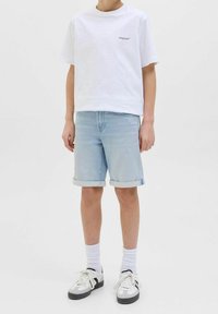 T-shirt bianca in cotone con stampa "Originals", pantaloni corti in denim azzurro chiaro con orlo risvoltato, calzini bianchi e sneaker grigie e nere.