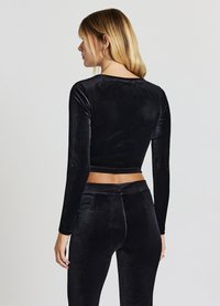 Top corto in velluto nero con maniche lunghe, texture liscia, collo tondo e design aderente, abbinato a pantaloni in velluto nero coordinati.