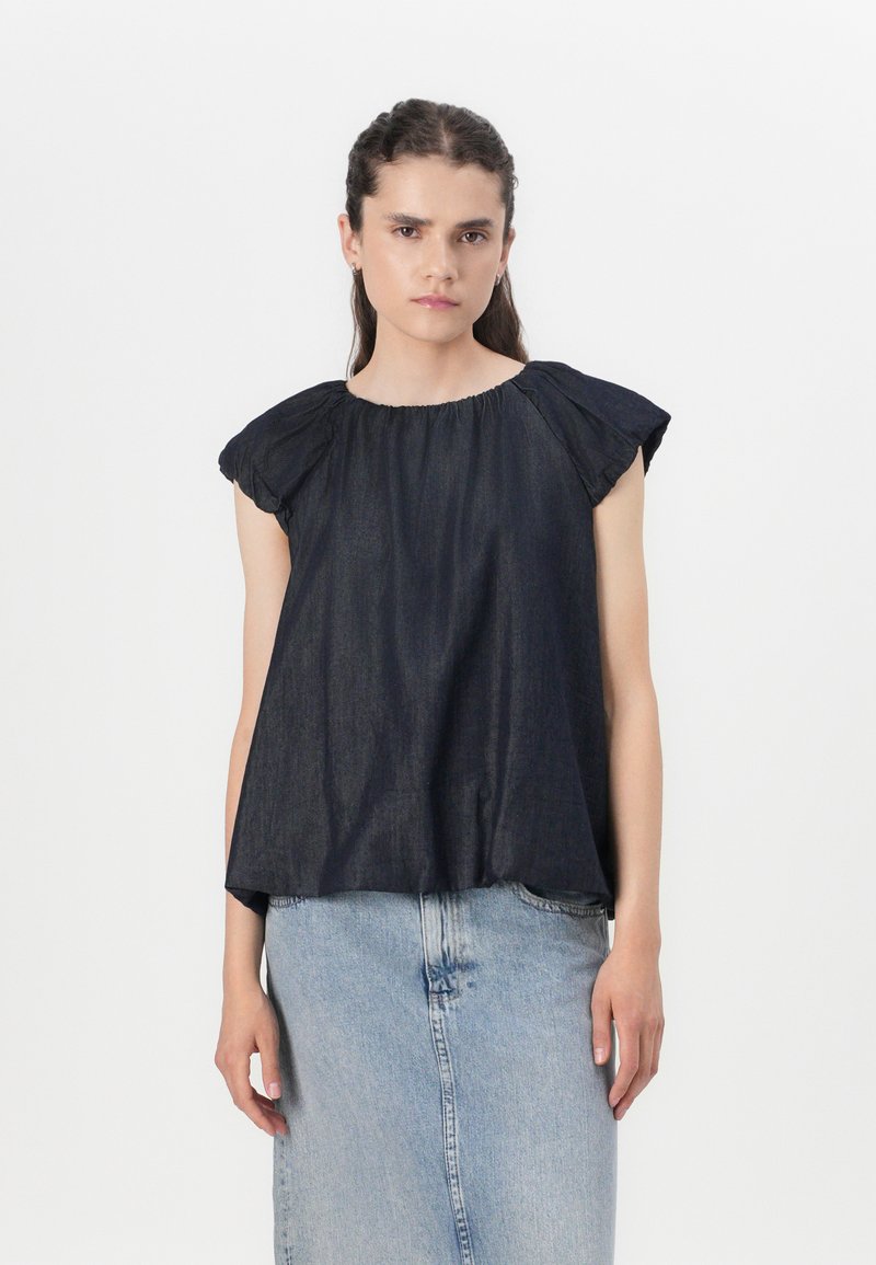 Mørkeblå denimtop med korte, rynkede ærmer, rund halsudskæring og afslappet pasform. Kombineret med en lyseblå denimnederdel.