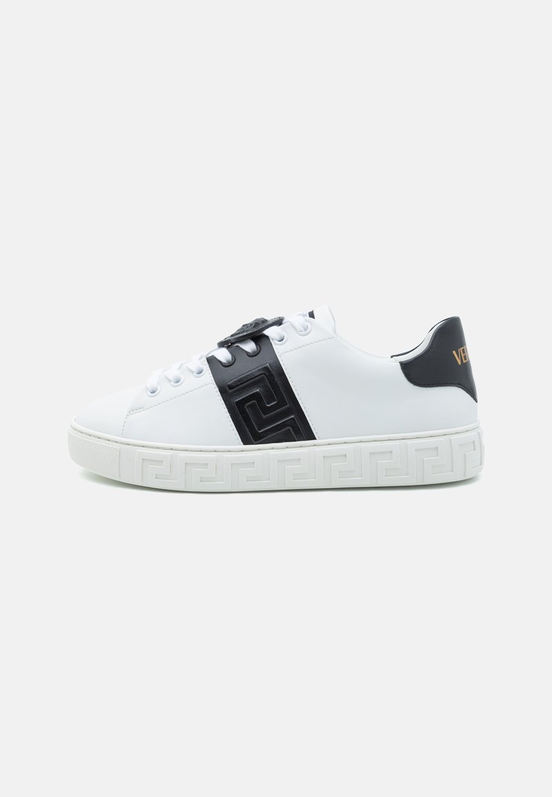 Sapatilha de couro branca com detalhes e logotipo em preto, sola com padrão de chave grega, atacadores planos e um detalhe em pele texturizada no calcanhar.