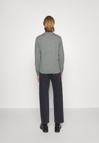 Grå genser med ribbet tekstur, rund hals, og lange ermer, kombinert med videre ben mørke jeans og svarte sko, sett fra baksiden.