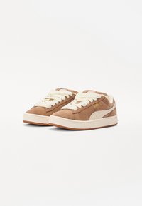 Brown suede sneakers with ivory laces and gum rubber soles. Features a side logo and textured accents on the sole. Classic low-top design.