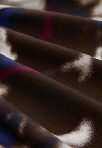 Mehrfarbiger Stoff mit dunkelbraunem Grund, der abstrakte Muster in Weiß, Lila und Blau zeigt, mit einer glatten, weichen Textur.