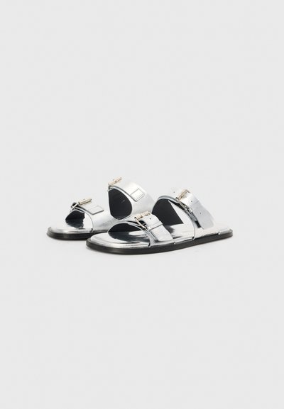 Sølvmetallic sandaler med to brede stropper, justerbare spænder, åben tå, flad sål og minimalistisk design. Glat tekstur.
