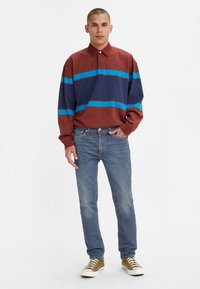 Camisa de manga larga color burdeos con rayas horizontales azules y navy, combinada con vaqueros de color azul claro y zapatillas de color verde olivo.
