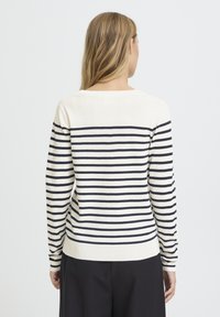 Pull rayé crème et bleu marine, avec un col rond et des manches longues. Tissu en maille douce avec un ourlet et des poignets côtelés.