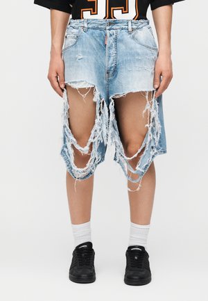 Person iført kraftigt slidte, revnede lyseblå cowboyshorts kombineret med hvide sokker og sorte sneakers.