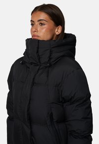 Giubbotto smanicato nero con colletto alto, caratterizzato da sezioni cucite e una tasca con zip sul lato sinistro. Texture liscia e trapuntata.