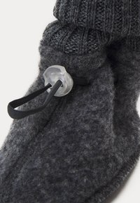 Grå ulltoffel med en stickad krage, utrustad med en plastspärr och svart snodd för justering. Mjuk, texturerad yta med en mysig design.
