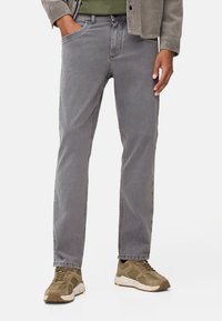 Grijze denim jeans met een rechte pasvorm, vijf zakken en gestikte details. Draagt een olijfgroene schoen en een gestructureerde grijze jas.