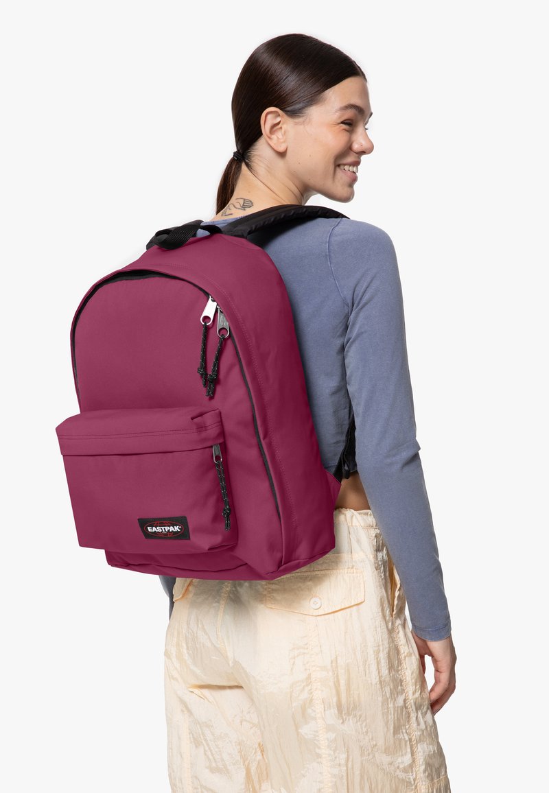 Mochila malva con un bolsillo frontal, cremalleras para el cierre, correas acolchadas y un parche con logo. Fabricada en tejido suave y duradero con un diseño elegante.