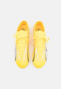 Zapatillas deportivas amarillas con un diseño elegante, material de malla, cordones prominentes y un patrón degradado de negro a blanco en los laterales.