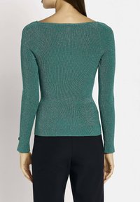 Teal ribbad topp med långa ärmar och bred rundad halsringning. Har texturerat tyg med metalliska accenter och en figurnära silhuett.