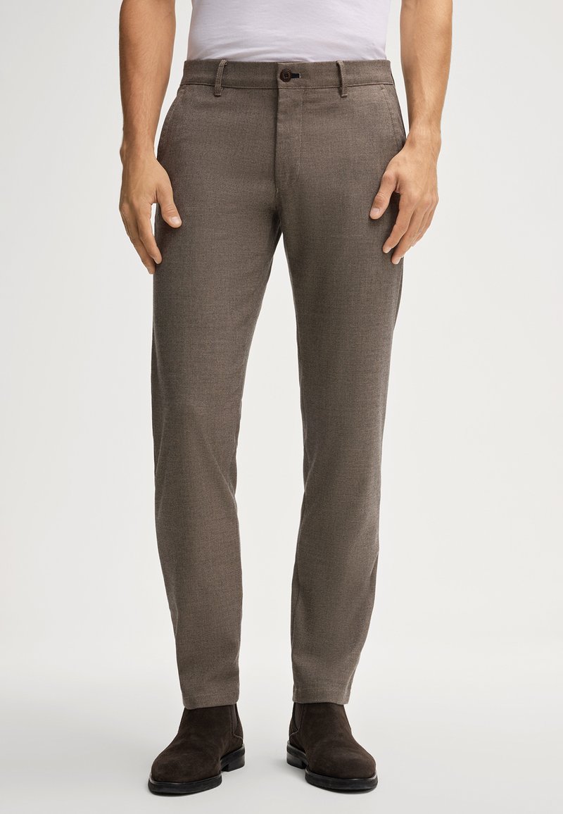 Pantaloni marroni con texture, slim fit, tasche frontali, chiusura con un bottone, abbinati a stivali alla caviglia marroni scuri.