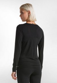 Zwarte langwerpige top met een aansluitend ontwerp, gemaakt van zachte stof. Heeft een ronde halslijn en een gedrapeerde achterkant met een lage zoom, minimale branding.