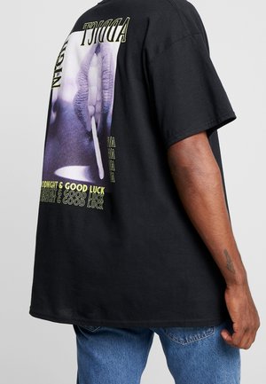 Schwarzes übergroßes T-Shirt mit Grafik von Lippen und Zigarette, darauf der Text "NIGHT ADDICT", "GOODNIGHT & GOOD LUCK", kombiniert mit blauer Jeans.