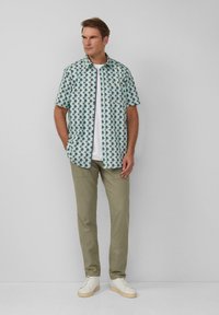 Korte mouwen shirt in licht turquoise met een palmbomenpatroon, gecombineerd met beige broek en witte sneakers. Soepele, casual uitstraling.
