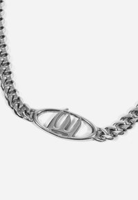 Brăţară din lanţ argintie cu linkuri interlocking şi un închizător oval cu un logo stilizat. Textură metalică netedă, finisaj lustruit.