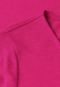 Gros plan d'un tissu rose vif montrant des coutures détaillées sur le bord replié d'une manche.