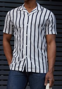 Kortärmelig overhemd met knopen in wit met marineblauwe verticale strepen, voorzien van een kraag en eenvoudige knopen, gecombineerd met blauwe spijkerbroeken.