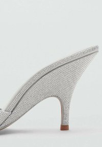 Scarpa con tacco alto argentata, rivestita di piccole strass, con punta affusolata e silhouette curva. Il tacco è in legno.