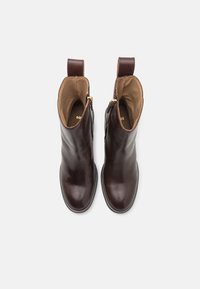Botas de cuero marrón hasta el tobillo con un acabado suave, cremalleras laterales y un tacón corto. Interior con forro beige y detalle del logo.