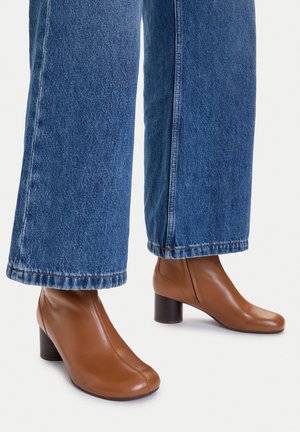 Brown leather ankle boots with block heels worn with wide-leg blue denim jeans against a white background.