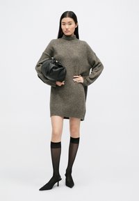 Üks suur hall-pruun kudum dress, millel on soonikuga varrukaotsad, on sobitatud mustade kõrge kontsaga kingade ja läbipaistvate mustade põlvikutega. Must kott on kaasas.