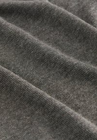 Grauer Strickstoff mit weicher Textur, der ein dezentes Rippenmuster und einen leichten Glanz aufweist, und Falten sowie Schichten zeigt.