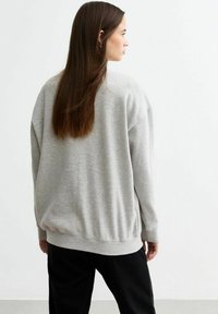 Felpa grigia con vestibilità rilassata, polsini e fondo a coste. Materiale in cotone morbido, cuciture minime e design leggermente oversize.
