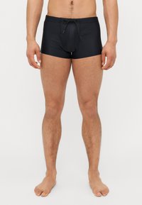 Shorts de bain noirs en tissu lisse, dotés d'une taille avec cordon de serrage, d'une coupe mi-cuisse et d'un design simple sans motifs ni logos.