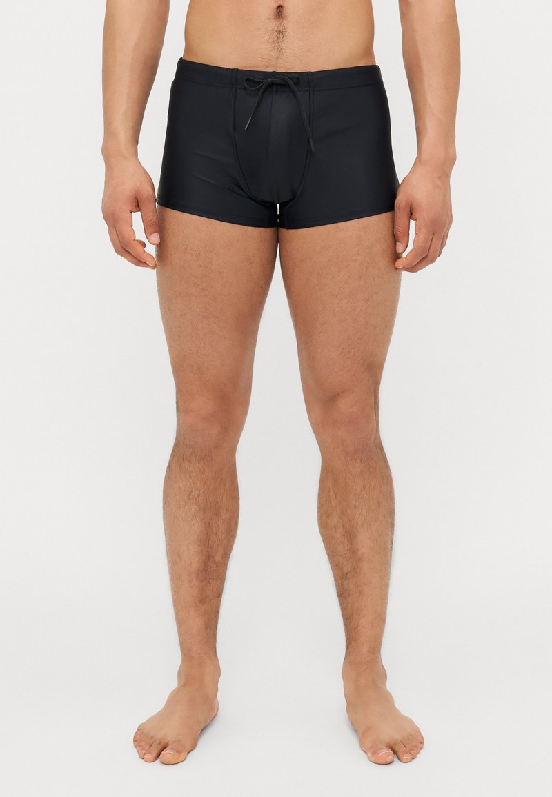 Shorts de bain noirs en tissu lisse, dotés d'une taille avec cordon de serrage, d'une coupe mi-cuisse et d'un design simple sans motifs ni logos.