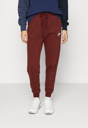 Persoon draagt bordeauxrode Nike joggingbroek met trekkoord en witte sneakers, gecombineerd met een marineblauw langermig shirt.