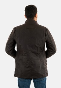 Bruine, waterdichte jas met een hoge kraag, lange mouwen en een getailleerde taille. Heeft een soepele textuur en een detail met een lus aan de achterkant.