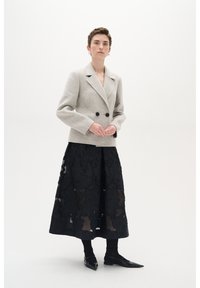 Grå uld dobbeltradet blazer med sorte knapper, parret med en sort midi-nederdel med et tekstureret mønster og gennemsigtige paneler.