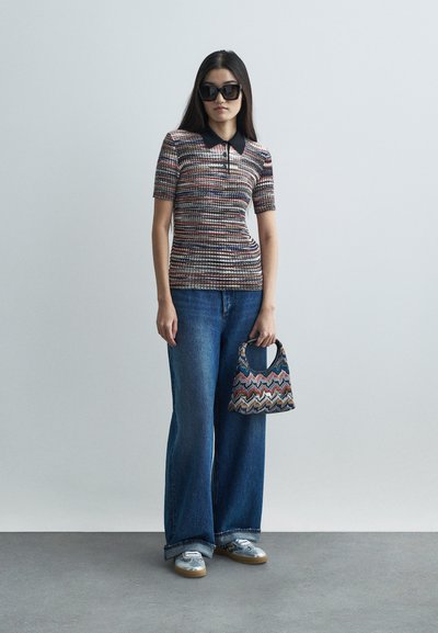 Polo en tricot à manches courtes, motif aux couleurs variées. Associé à un jean bleu à jambe large et un sac à main zébré multicolore.
