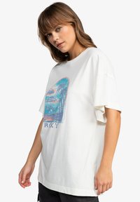 Bílý oversized tričko s barevným grafikou palem a vody. Má krátké rukávy a uvolněný střih. Měkký bavlněný materiál.