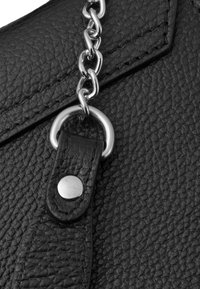 Dettaglio di una borsa in pelle nera con texture, caratterizzata da un accento in catena argentata e un pulsante a scatto su un cinturino in pelle per una chiusura sicura.