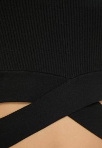 Svart ribbat tyg med en texturerad yta, med korsande accenter och en åtsittande form. Minimalistisk design utan synlig hårdvara eller mönster.