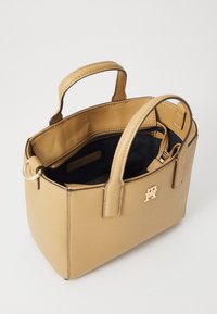 Sac à main en cuir tan avec deux poignées supérieures et des finitions en or. L'intérieur présente une doublure noire et un compartiment zippé. Forme carrée.