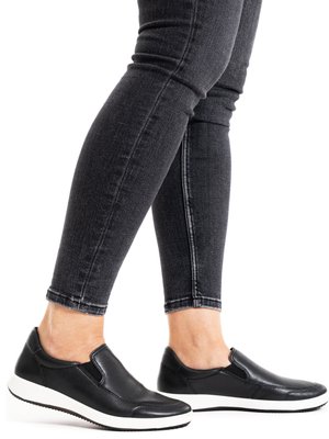 Legs wearing black skinny jeans and black slip-on sneakers with white soles against a white background.
