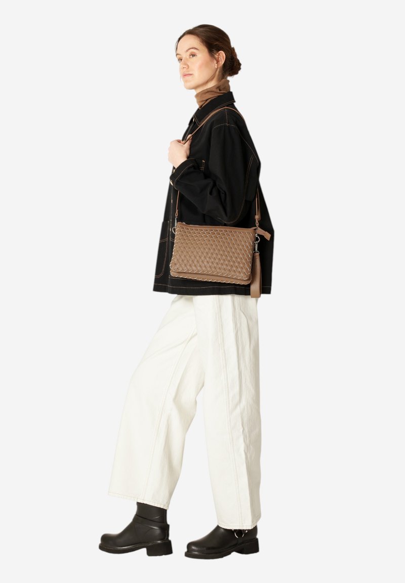 Woven brown leather crossbody bag with a structured rectangular shape, featuring a tassel accent and adjustable strap, worn with white pants.