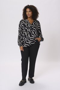 Blouse à motifs noir et blanc avec un décolleté en V et des manches amples, accompagnée d'un pantalon noir et de chaussures noires ornées d'un accent doré.