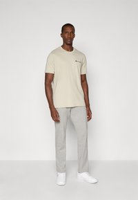 Lys beige t-shirt med rund hals og lille logo, parret med lysegrå sweatpants og hvide sneakers. Blødt bomuldsblandingsstof.