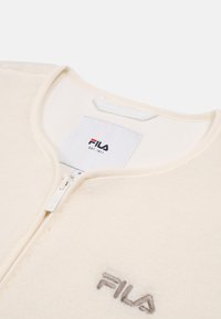 Giacca in pile color crema con chiusura a zip, marchio Fila in grigio chiaro, scollo rotondo e texture liscia. Design leggero e confortevole.