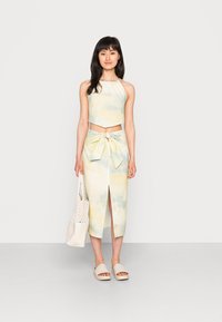 Conjunto de duas peças com um top crop halter e uma saia midi com uma fenda à frente. O tecido tem um padrão de tie-dye em amarelo claro e azul.